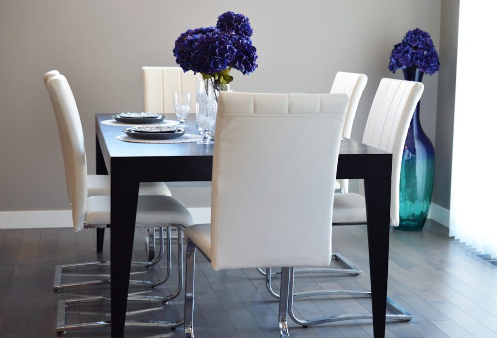 A stylish, contemporary dining room featuring elegant white chairs and a dark wooden table adorned with purple flowers.